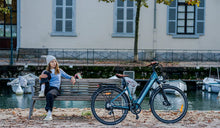 A woman sits on a park bench and looks at a Fiido C11pro electric bicycle