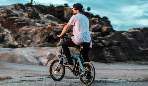 A cyclist on the Fiido D11 exploring a rocky coastal terrain at sunset.