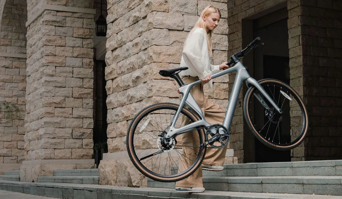 A woman effortlessly lifts a Fiido Air lightweight electric bike up the stairs.